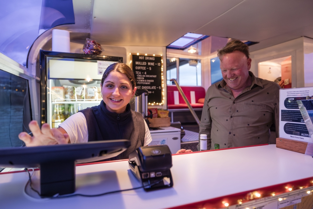 Smiling cashier serving a happy customer on a cruise.